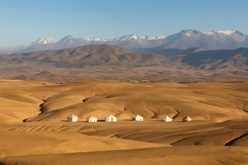 Desert dunes with a small tented camp and snow-capped Atlas Mountains in Morocco
