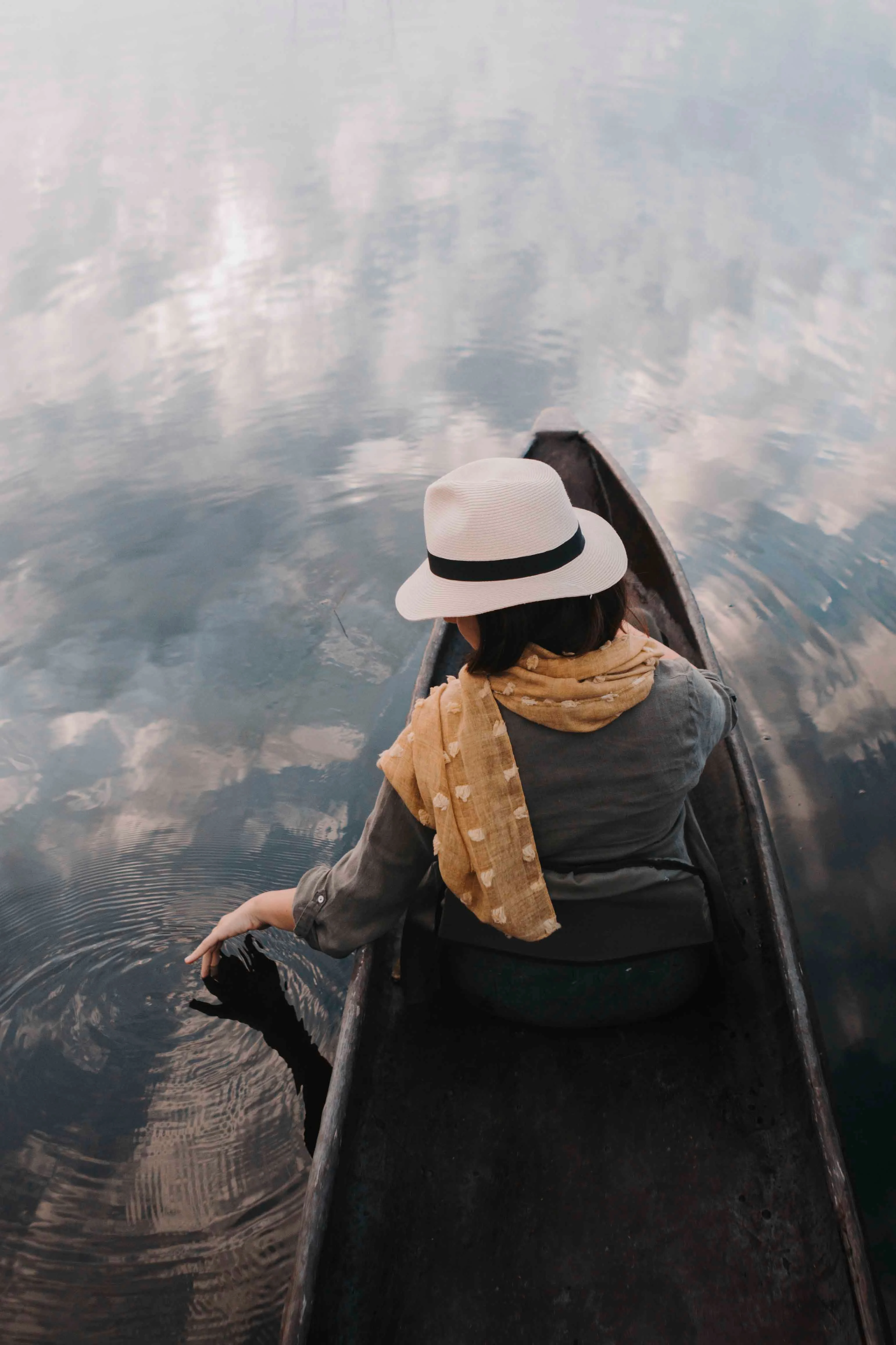Solo traveller in a sun hat, seen from behind, in a small boat on still water